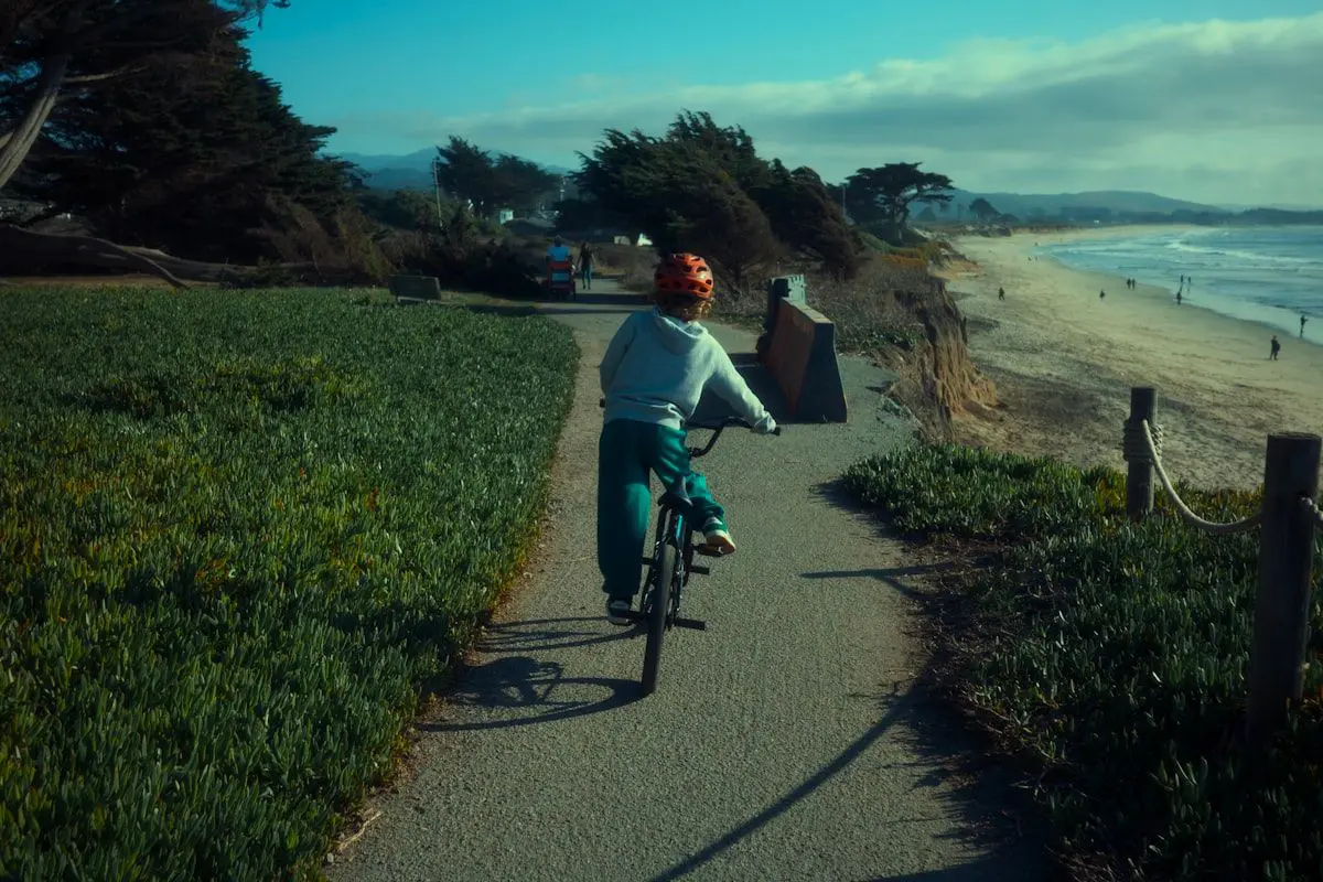 A side-by-side view of a regular cruiser bike and an e-bike on a quiet coastal path, showing the e-bike’s battery mounted on the frame and a rider cruising easily with one hand on the handlebars